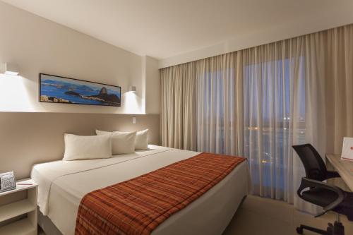 a hotel room with a bed and a window at Ramada by Wyndham Macae Hotel & Suites in Macaé