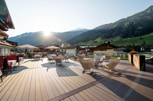 a deck with chairs and tables with mountains in the background at Premium Activehotel Bergkönig in Neustift im Stubaital