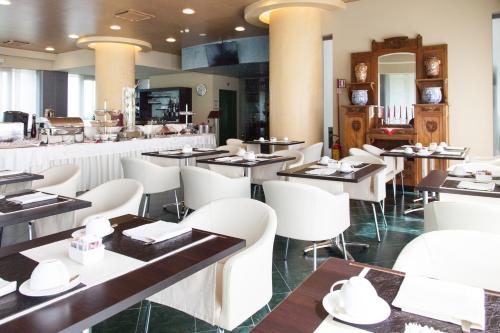 un ristorante con tavoli, sedie bianche e bancone di Hotel Senator a Gorgonzola