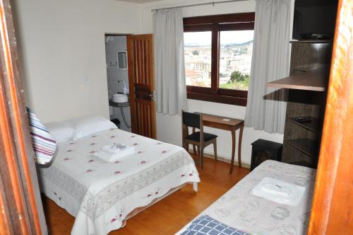a bedroom with a bed and a table and a window at Pousada Monte Carlo in São Joaquim