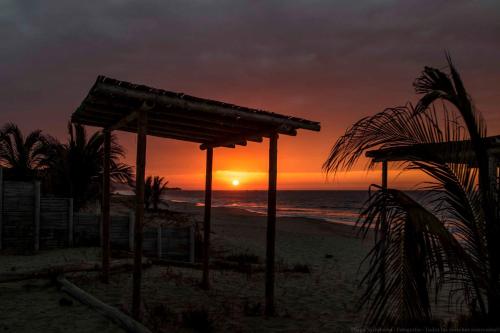 una puesta de sol en la playa con una cabaña de madera en Mamaqocha, en Canoas de Punta Sal