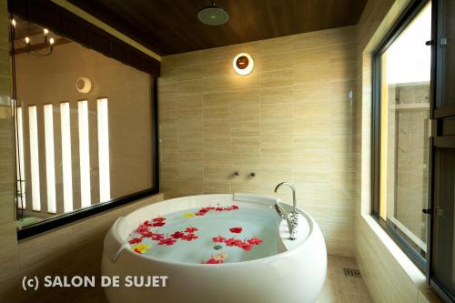 un baño con una bañera blanca con flores rojas. en Bougain Terrace Resort Thi-chi House en Nago