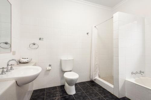 a white bathroom with a toilet and a sink at The International Motel Apollo Bay in Apollo Bay