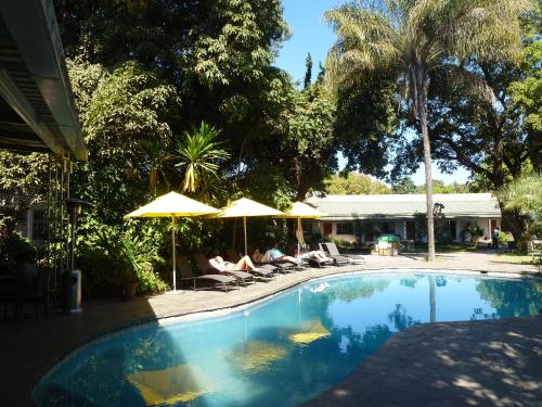 a swimming pool with two people sitting under umbrellas at Fawlty Towers Accommodation & Activities in Livingstone