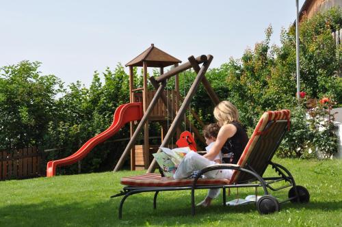 two women sitting in a chair next to a playground at Pension Wiesenrain in Maranza