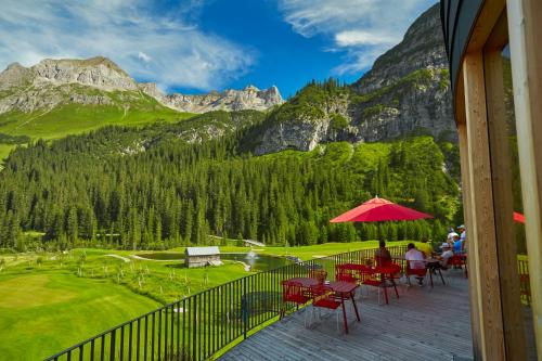 a deck with tables and chairs and a red umbrella at Hotel Appartement Roggal in Lech am Arlberg