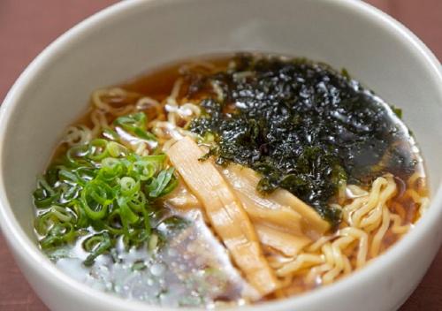 a white bowl of soup with noodles and greens at Dormy Inn Express Matsue in Matsue