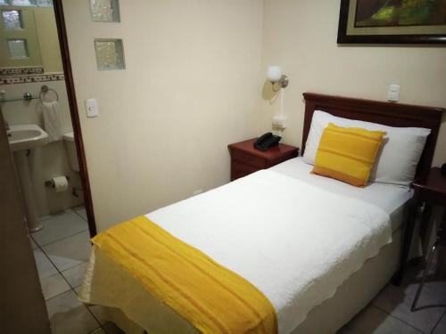 a bedroom with a bed with a yellow pillow and a sink at Hotel San Jose Hostal in San Salvador