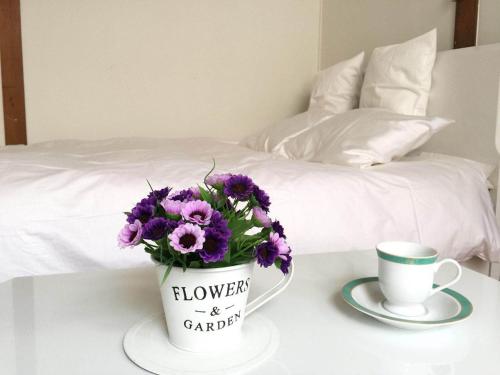a vase of purple flowers on a table with a cup at Happy Apartment in Sapporo
