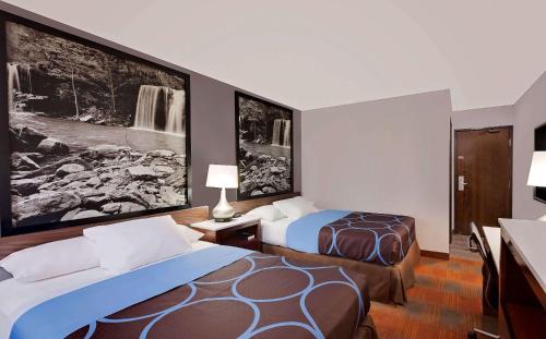 Habitación de hotel con 2 camas y pinturas en las paredes. en Super 8 by Wyndham Fayetteville, en Fayetteville