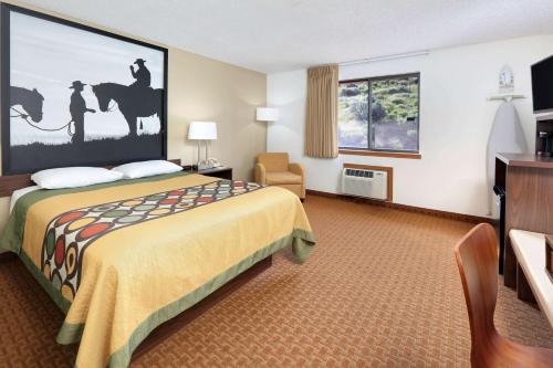 a hotel room with a bed and a chair and window at Super 8 by Wyndham Cody in Cody
