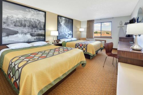 a hotel room with two beds and a desk at Super 8 by Wyndham Cody in Cody