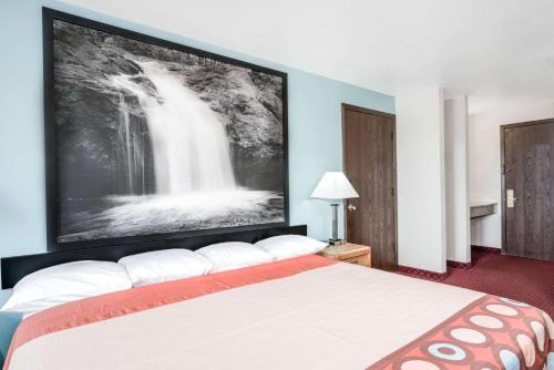 a hotel room with a bed with a large painting on the wall at Super 8 by Wyndham Tomah Wisconsin in Tomah