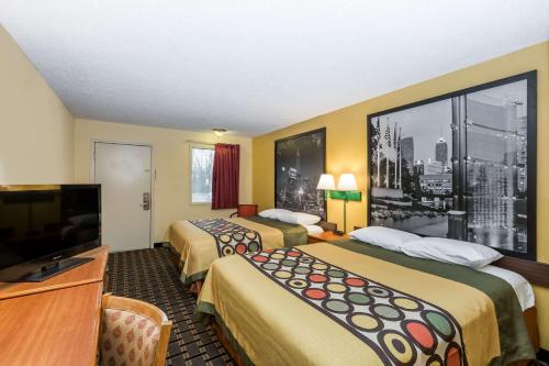 a hotel room with two beds and a flat screen tv at Super 8 by Wyndham Indianapolis-Southport Rd in Indianapolis