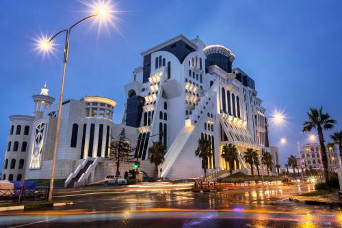 a large white building with palm trees and a street at The Grand Gloria Hotel in Batumi