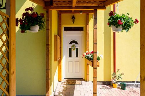 a yellow building with a white door and two potted plants at Bakterház Vendégház in Nagyvisnyó