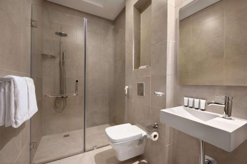 a bathroom with a shower and a toilet and a sink at Ramada Encore by Wyndham Kuwait Downtown in Kuwait
