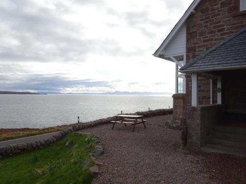 a picnic table sitting outside of a building next to the water at Gairloch Sands Youth Hostel in Gairloch