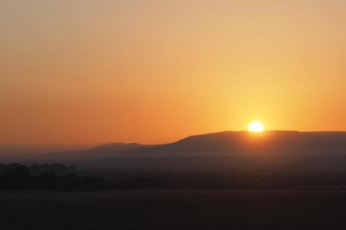 a sunset over the mountains with the sun setting on the horizon at Basecamp Wilderness in Naboisho