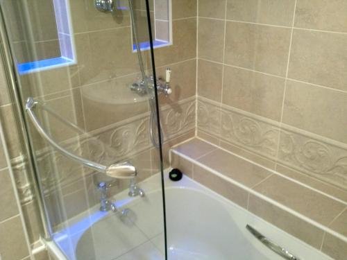 a shower with a glass door next to a bath tub at Rogerthorpe Manor Hotel in Pontefract