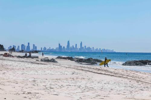 a man walking on the beach with a surfboard at Sandbox Apartments in Gold Coast