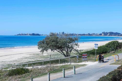 a woman walking down a road next to a beach at Sandbox Apartments in Gold Coast