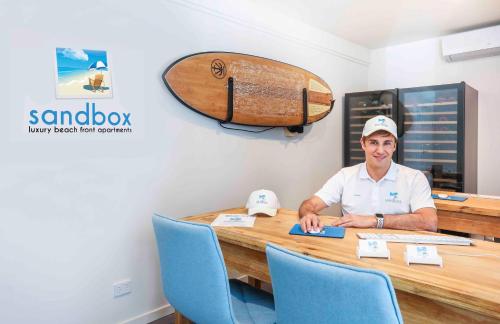 a man sitting at a table with a surfboard on the wall at Sandbox Apartments in Gold Coast
