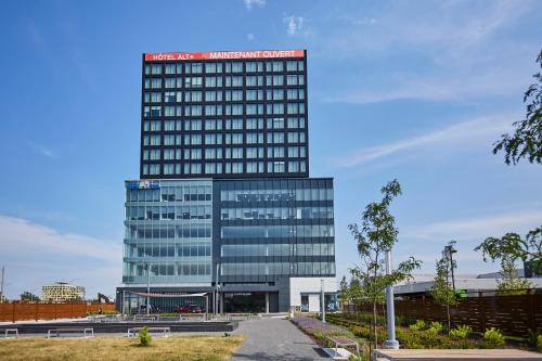 a tall glass building with a red sign on it at Hôtel Escad Quartier DIX30 in Brossard