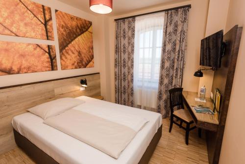 a bedroom with a bed and a desk and a window at JUFA Hotel Fürstenfeld in Fürstenfeld
