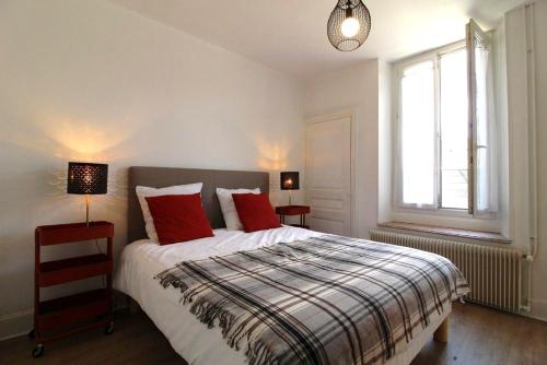 a bedroom with a bed with red pillows and a window at Appartements Le Cru Colbert in Beaune