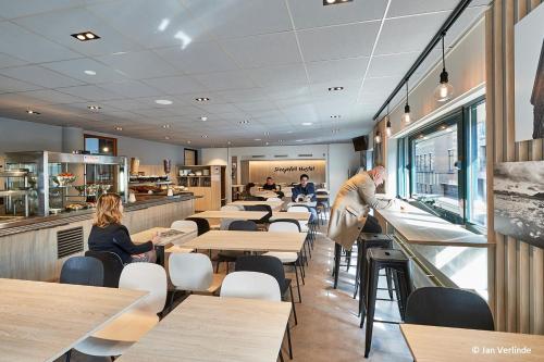 um restaurante com mesas e cadeiras e um homem a preparar comida em Sleep Well Youth Hostel em Bruxelas