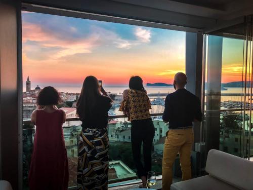 a group of people standing on a balcony looking out at the sunset at Hotel Catalunya in Alghero