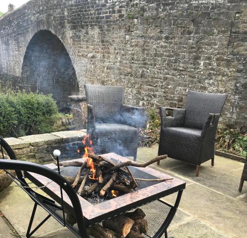 BainbridgeにあるBridge Cottage, Bainbridge, with riverside garden!の煉瓦の壁前の椅子2脚と火炉