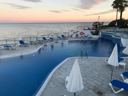 a swimming pool with chairs and umbrellas next to the ocean at Dominion Beach House in Estepona