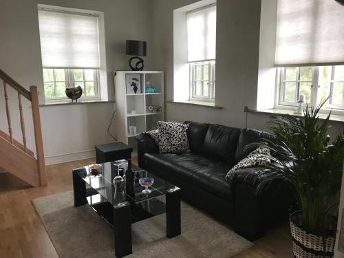 a black leather couch in a living room with windows at Centralt i Gentofte i 2 plan, ved S-Tog og busser in Gentofte