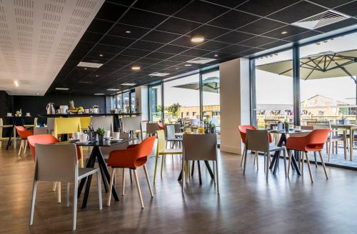 a restaurant with tables and chairs and windows at Najeti Hôtel Lille Nord in Bondues