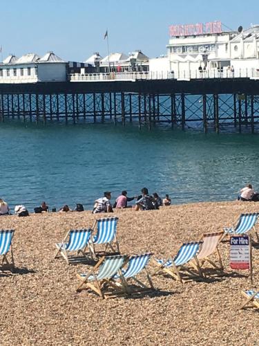 people sitting in lawn chairs on a beach with a pier at Kemp Town Sea View Balcony Apartment in Brighton & Hove