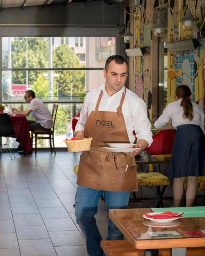 a man wearing an apron holding a plate in a restaurant at Hotel Lirak in Tetovo