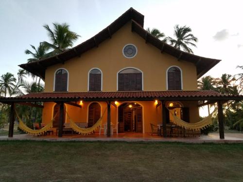 a large yellow house with hammocks in front of it at Pousada Igrejinha dos Carneiros in Tamandaré