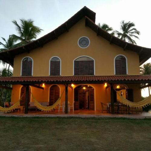 a large yellow house with hammocks in front of it at Pousada Igrejinha dos Carneiros in Tamandaré