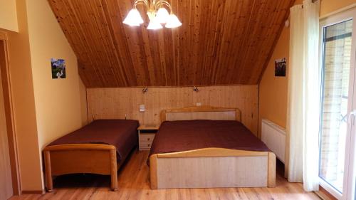 two beds in a room with wooden ceilings and a window at Raudonkalnis in Mankiškiai