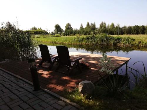 two chairs sitting on a wooden deck next to a pond at Raudonkalnis in Mankiškiai
