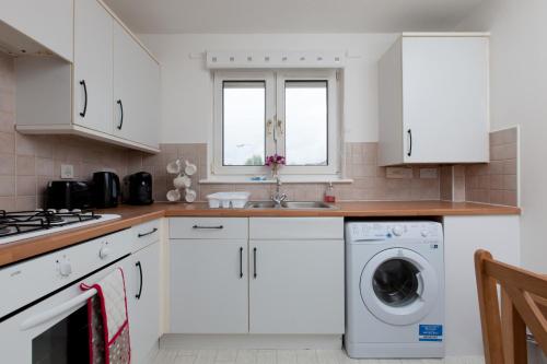 eine Küche mit weißen Schränken, einer Waschmaschine und einem Trockner in der Unterkunft Prime Commuter Executive Apartment Dunfermline in Dunfermline