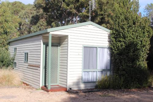 a small white shed with a window next to a bush at The Lakes Beachfront Holiday Park in Lakes Entrance