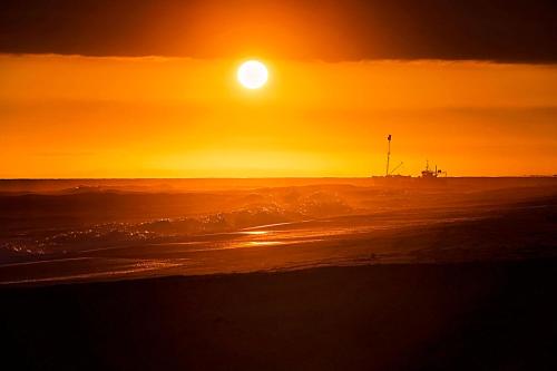 a sunset on the beach with a boat in the ocean at The Lakes Beachfront Holiday Park in Lakes Entrance