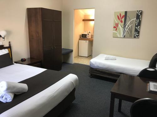 a hotel room with two beds and a desk at Hideaway Motor Inn in Armidale