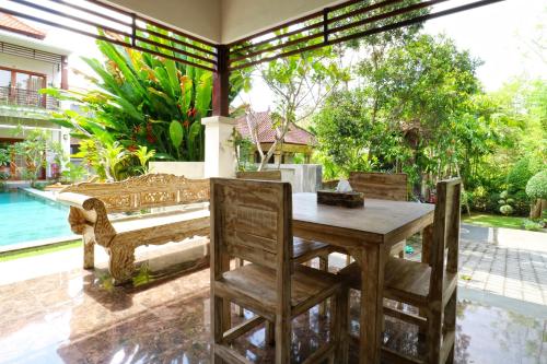 een houten tafel en stoelen op een patio met een zwembad bij Avisara Villa & Suite in Nusa Dua