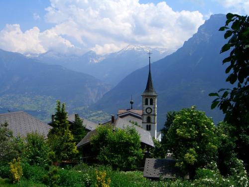 a church with a clock tower with mountains in the background at Bergquell Haus D in Blatten bei Naters