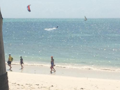 a group of people walking on a beach flying a kite at Jaribu Beach Hotel in Paje