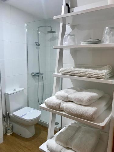 a white bathroom with a toilet and towels on shelves at Hostal Puerta La Villa in Tordesillas